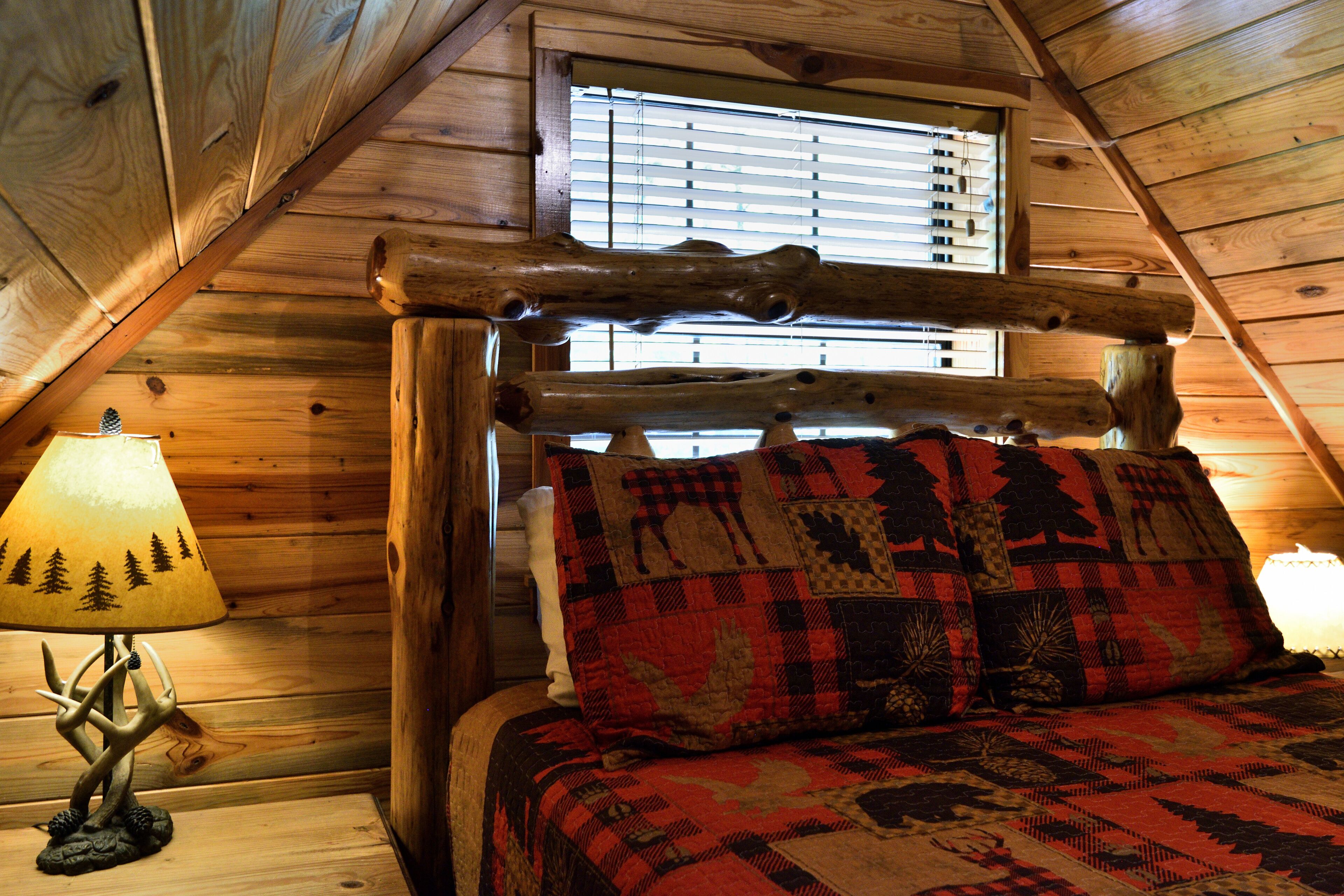 Interior de una cabaña de madera con una cama, una lámpara y una ventana con persianas.