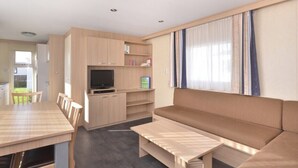 Ein modernes Wohnzimmer mit einer Couch, einem Fernseher, Holzsärchen und einem Esstisch.