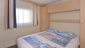 Ein Schlafzimmer mit Bett, einem Fenster mit Vorhängen und Holzschränken.