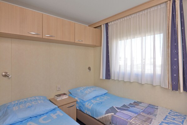 A compact bedroom with two single beds, a small bedside table, and a wardrobe.