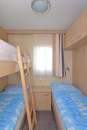 A compact bedroom with bunk beds, a small desk, and a window with curtains.