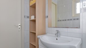 Ein Badezimmer mit einem weißen Waschbecken, Holzregalen und einem Spiegel.