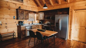 A wooden cabin kitchen with a wooden table, chairs, a refrigerator, a microwave, and a coffee maker. - Amazing mountain view!5-star cabin,Modern,Minutes to BR&EJ,Hot tub,Games (Blue Ridge)