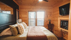 A wooden cabin bedroom with a bed, a ceiling fan, a TV, and a fireplace. - Amazing mountain view!5-star cabin,Modern,Minutes to BR&EJ,Hot tub,Games (Blue Ridge)