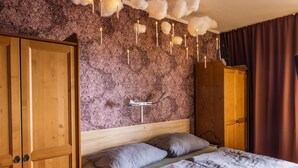 A bedroom with a wooden wardrobe, a bed with grey bedding, a patterned wallpaper, and a ceiling with hanging lights. - Muggles welcome: Harz time-out in the Zauberquartier with sauna and swimming pool (Braunlage)