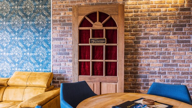 A cozy room with a brick wall, a wooden door with a sign, a round wooden table, and two blue chairs. - Muggles welcome: Harz time-out in the Zauberquartier with sauna and swimming pool (Braunlage)