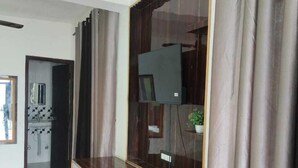 Une pièce avec un meuble en bois, un téléviseur et une salle de bain visible à travers une porte ouverte.