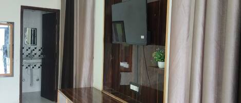 Une pièce avec un meuble en bois, un téléviseur et une salle de bain visible à travers une porte ouverte.
