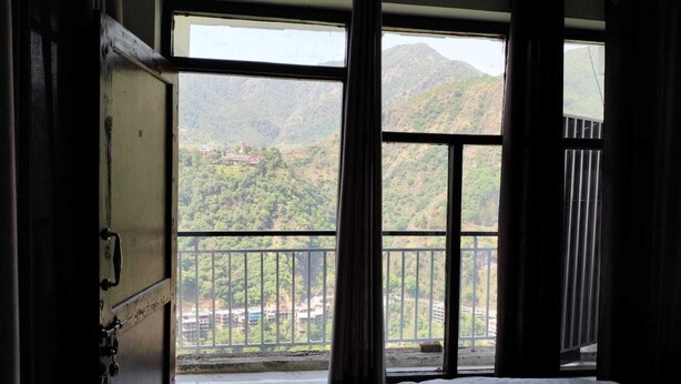 Une chambre avec un lit, une fenêtre donnant sur un paysage montagneux et un balcon avec une balustrade.