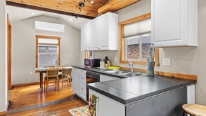 A modern kitchen with white cabinets, a central island, and a dining area with wooden chairs. - Walkable Urban Retreat. Remodeled 1920 Gem in Heart of Midtown-Walk to Breweries (Reno)