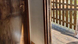 A wooden door with a fish-shaped decoration, a view of a wooden deck, and a wooden fence overlooking a landscape with trees and hills. - Bungalow Sixdays 3 with outdoor hot tub. (Camporosso)