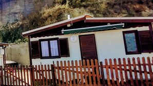 A building with a wooden fence in the foreground, a white wall, and a window with a curtain. - Bungalow Sixdays 3 with outdoor hot tub. (Camporosso)