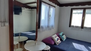 A room with a bed, a table with chairs, a mirror, and a window with curtains. - Bungalow Sixdays 3 with outdoor hot tub. (Camporosso)
