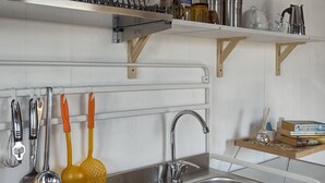 A kitchen with white cabinets, a stainless steel sink, and various utensils hanging on the wall. - Bungalow Sixdays 3 with outdoor hot tub. (Camporosso)