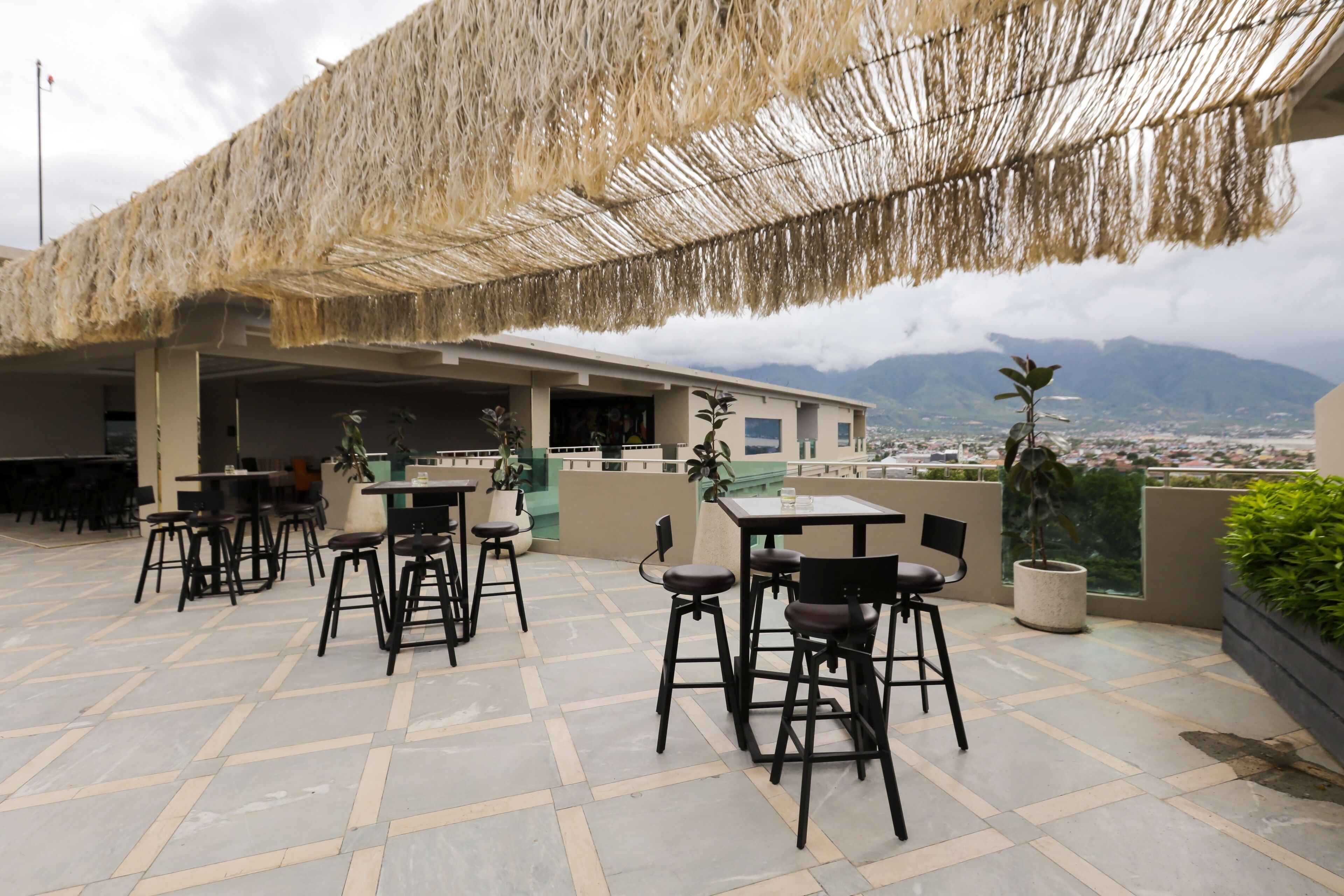 Un espace extérieur aménagé avec des tables et des chaises, un toit de chaume et une vue sur les montagnes lointaines.