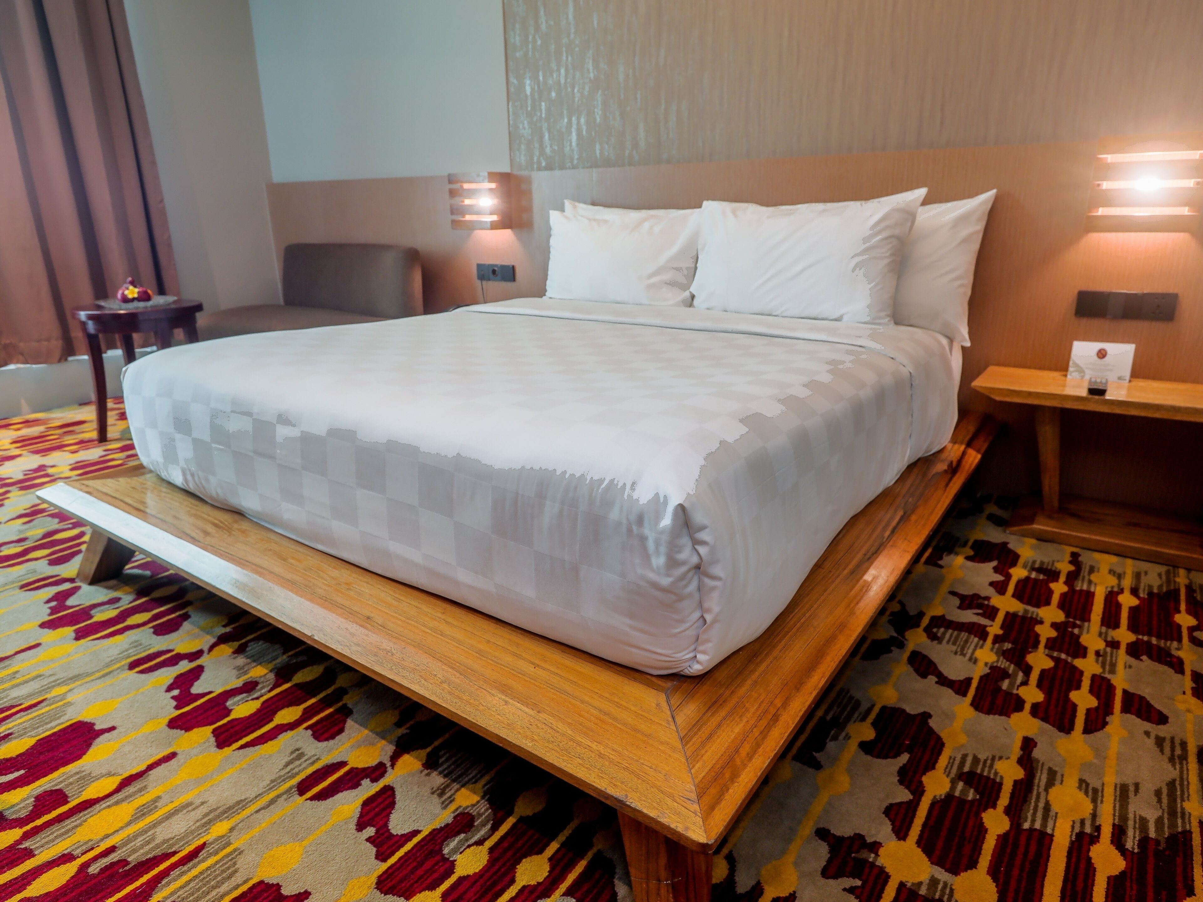 Ein Hotelzimmer mit einem großen Bett, einem hölzernen Kopfteil, einem gemusterten Teppich und einem kleinen Tisch mit einer Lampe.