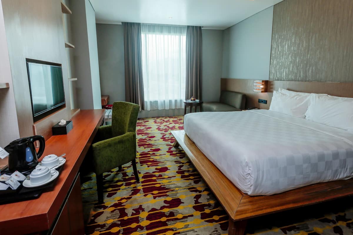 Een hotelkamer met een bed, een bureau met koffiezetapparaat, een stoel, een televisie en een raam met gordijnen.
