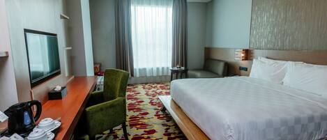 A hotel room with a bed, a desk with a coffee maker, a chair, a TV, and a window with curtains.