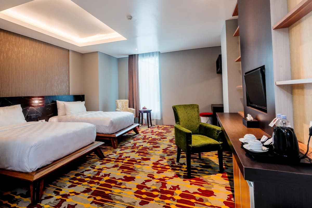 Een hotelkamer met twee bedden, een groene fauteuil, een bureau met een televisie en een kamerbreed tapijt met een patroon.