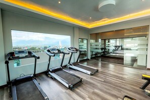 Une salle de sport moderne équipée de tapis de course, dotée d’une grande fenêtre offrant une vue sur la ville et bénéficiant d’un aménagement spacieux.