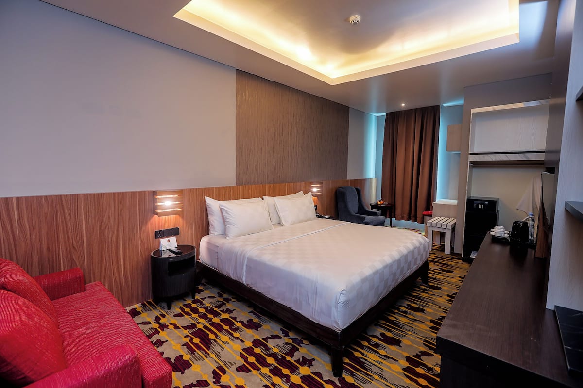Een hotelkamer met een bed, een rode bank, een bureau, een stoel en een klein tafeltje.