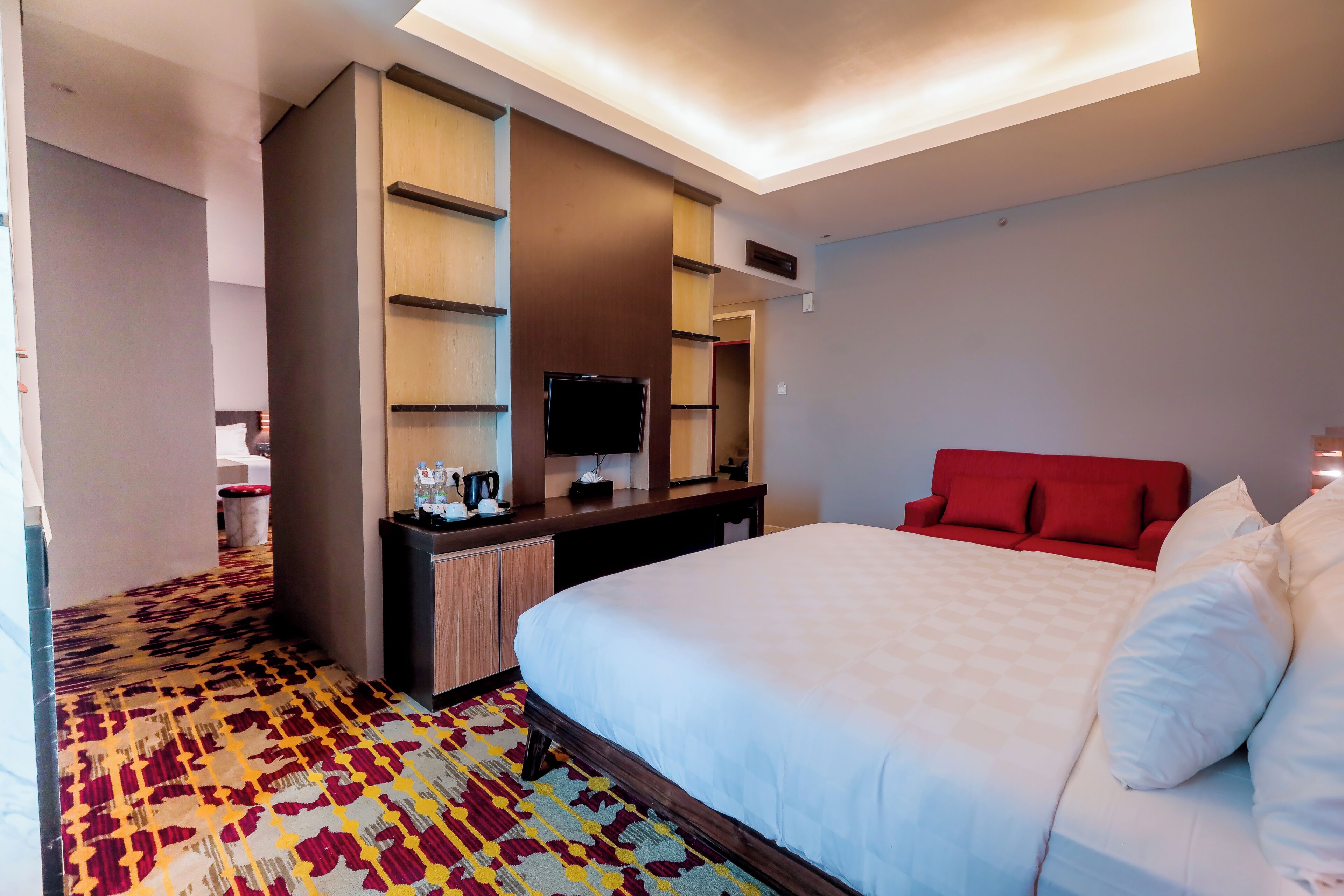 Une chambre d’hôtel avec un grand lit, un bureau doté d’un téléviseur à écran plat, un canapé rouge et une moquette à motifs.