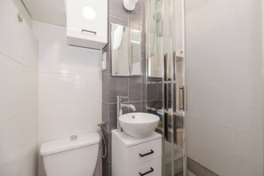 Un baño moderno con inodoro blanco, un lavabo blanco y un espejo encima, y una cabina de ducha con paredes de vidrio.