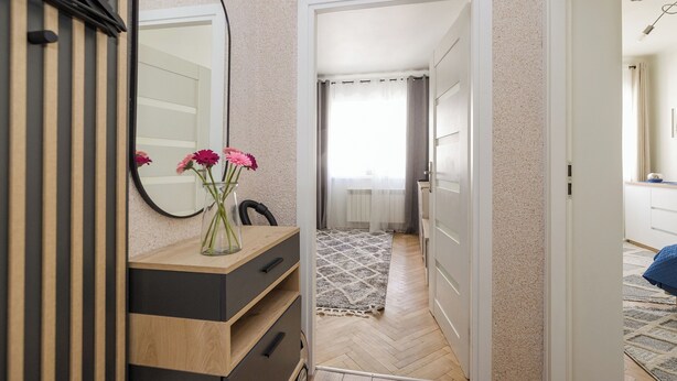 A bedroom with a wooden dresser, a mirror, and a vase with flowers. - ShortStayPoland Nowolipie B182 (Warsaw)