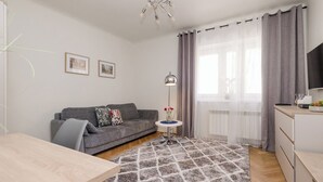 A modern living room with a grey sofa, a small round table with a vase of flowers, a floor lamp, and a large window with grey curtains. - ShortStayPoland Nowolipie B182 (Warsaw)