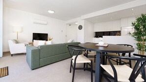 A modern living room with a green sofa, a round dining table, and a kitchen in the background.