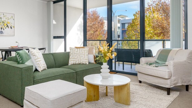 A modern living room with a green sofa, a white armchair, and a round coffee table with a vase of flowers.