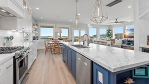 Une cuisine moderne avec des armoires blanches, un grand îlot central et une vue sur l’océan.