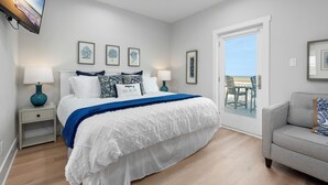 Une chambre à coucher avec un lit, des tables de chevet, une télévision et une vue sur l’extérieur, visible à travers une porte vitrée.