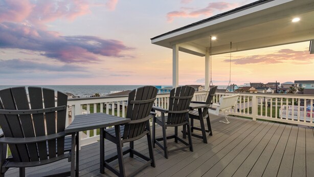 Une terrasse dotée de chaises Adirondack et d’une table, offrant une vue sur une étendue d’eau avec des bâtiments en arrière-plan.