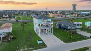 Un quartier résidentiel situé sur la côte, avec une imposante maison à deux étages dotée d’un balcon et, en arrière-plan, d’un château d’eau.