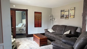 A living room with a brown leather sofa, a wooden chest, and a gray carpet.