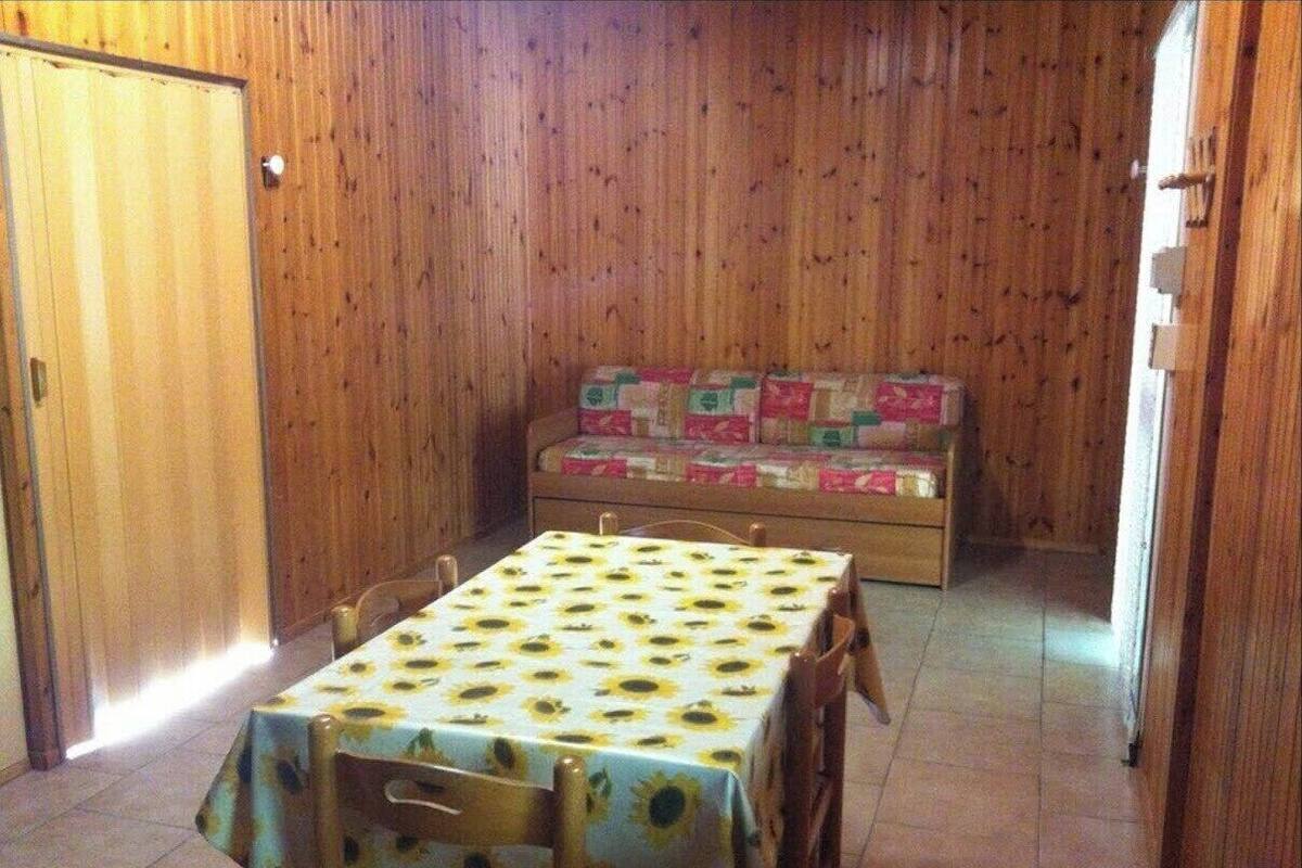 Una habitación con un panel de madera, una mesa con mantel de girasol, un banco con cojín colorido y una puerta.