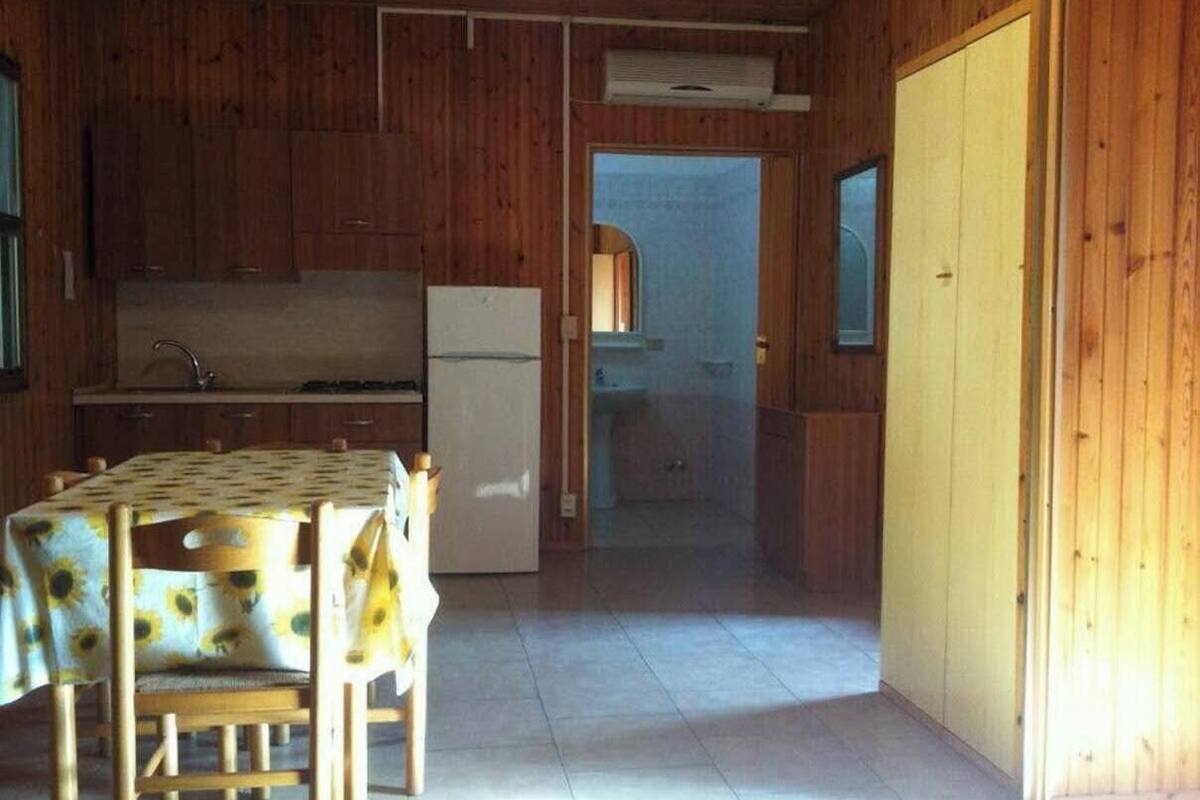Un interior de madera con una cocina, una mesa de comedor con mantel de girasol y una puerta que da a otra habitación.
