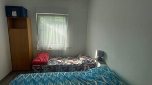 A small room with a bed, a wardrobe, a window with sheer curtains, and a bedside lamp. - Surrounded by nature, cozy apartment with private garden and grill area (Novaledo)