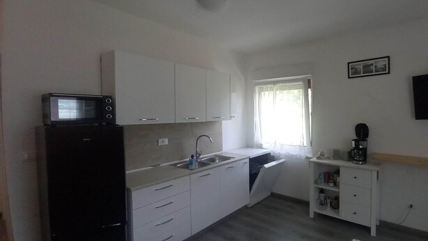 A compact kitchen with white cabinets, a built-in microwave, a sink, and a coffee maker. - Surrounded by nature, cozy apartment with private garden and grill area (Novaledo)