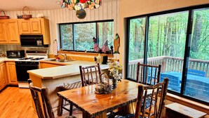 A kitchen with wooden cabinets, a stove, and a large window overlooking a deck. - Treehouse on the Lake! Direct Lakefront Home with Private Dock on Lake Glenville (Cullowhee)
