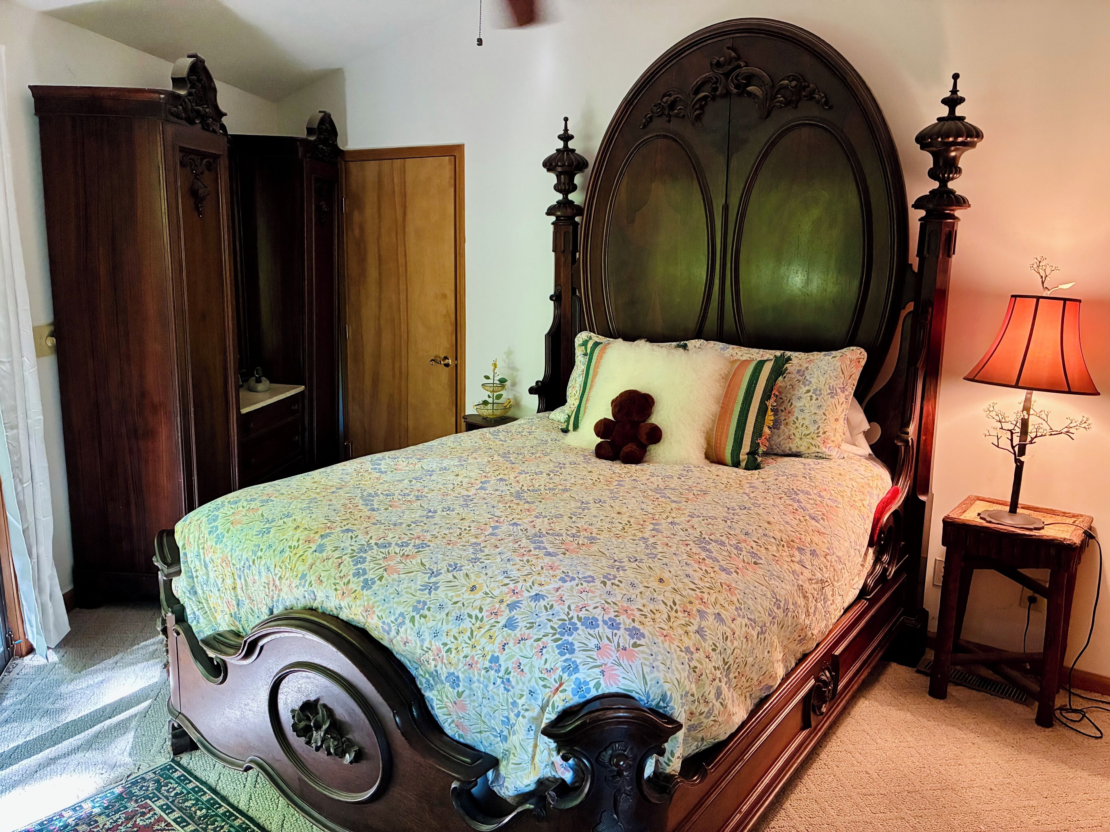 A classic four-poster bed with floral bedding, a wooden wardrobe, and a bedside lamp.