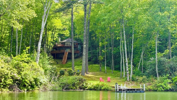 A cabin with a deck and a dock extending into a lake, surrounded by dense forest. - Treehouse on the Lake! Direct Lakefront Home with Private Dock on Lake Glenville (Cullowhee)