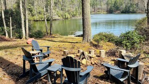 A lakeside seating area with Adirondack chairs and a fire pit. - Treehouse on the Lake! Direct Lakefront Home with Private Dock on Lake Glenville (Cullowhee)