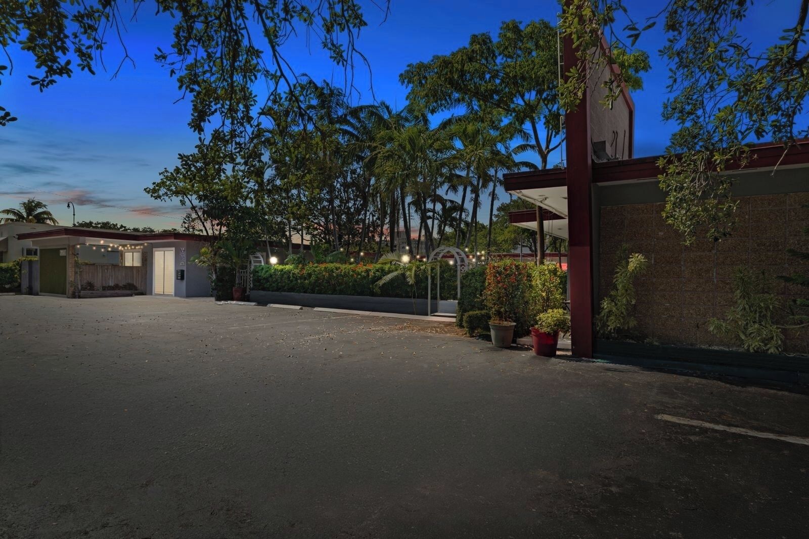 A parking lot with a building entrance, surrounded by trees and a clear sky.