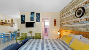 Una camera da letto con un letto, una TV, una parete in legno e un bagno visibile attraverso una porta aperta.