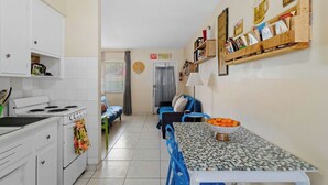 Una cucina compatta con mobili bianchi, un fornello e un'area pranzo con tavolo a scacchi e sedie blu.