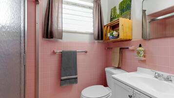 Un baño con baldosas rosas, un inodoro blanco, un lavamanos con espejo y una ventana con cortinas.