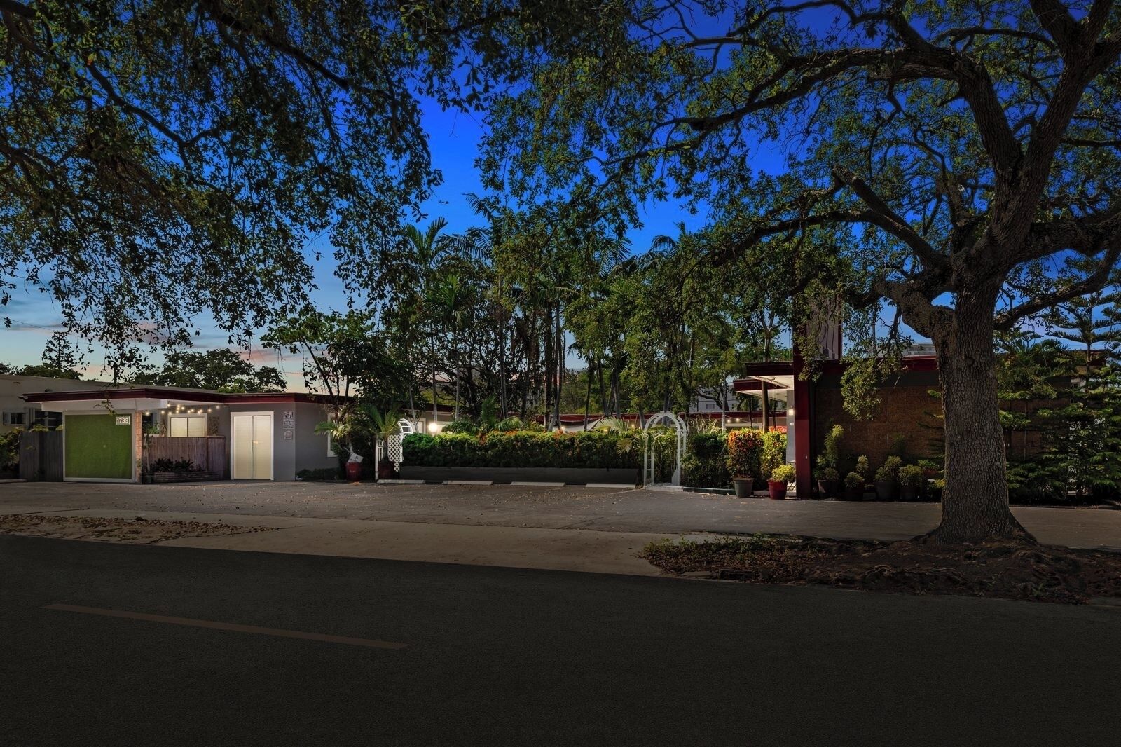 A modern building with a covered entrance, a parking area, and a tree in the foreground.