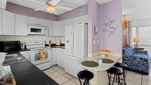 A compact kitchen with white cabinets, a microwave, an oven, and a refrigerator. There is a dining area with a table and two bar stools.